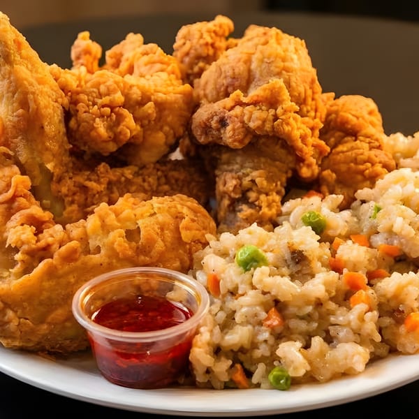 A plate of crispy fried chicken, vegetable fried rice, and a side of red dipping sauce.