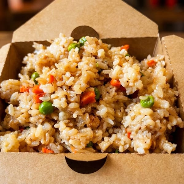 Fried rice with peas and carrots in an open brown takeout container on a wooden table.