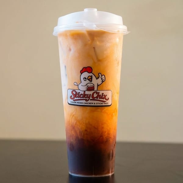 Thai iced tea in a clear plastic cup with the "Sticky Chix" logo on a dark surface.