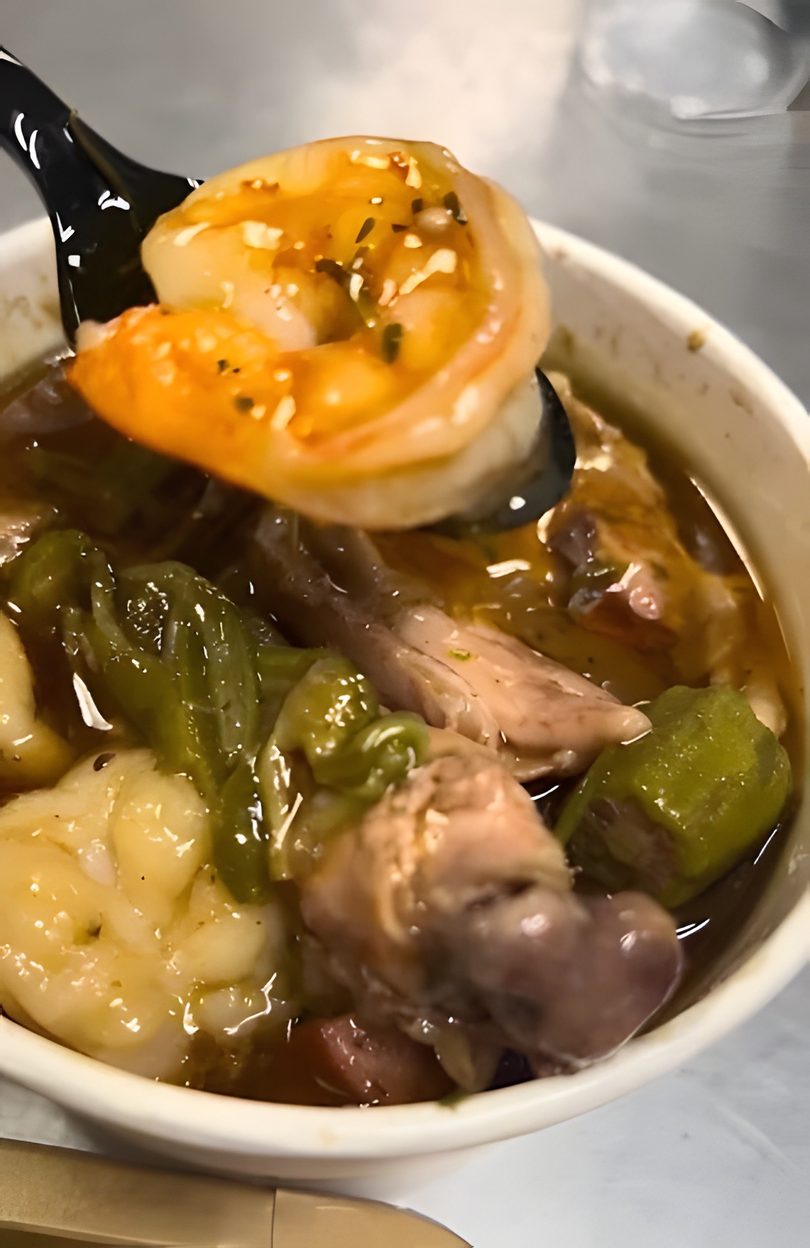 Close-up of a spoonful of gumbo with shrimp, chicken, and okra in a white bowl.