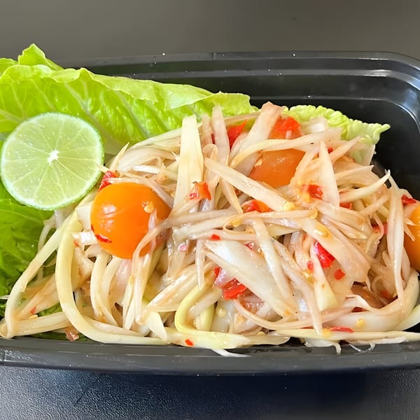 Som Tum (papaya salad) with lime, cherry tomatoes, and lettuce in a black container.
