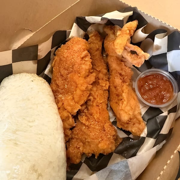 Fried chicken tenders, white rice, and a side of sauce in a takeout box with checkered paper.