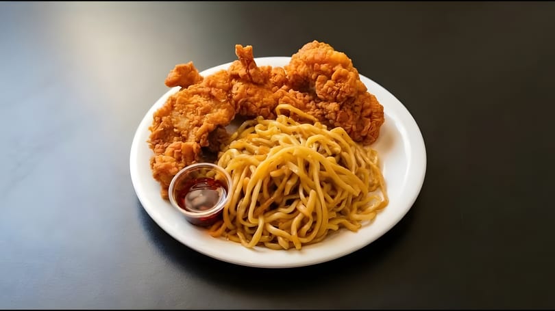 Crispy fried chicken pieces and a pile of noodles with a side of sauce on a white plate.