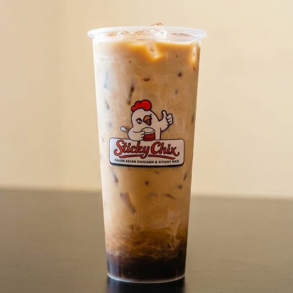 Iced coffee in a clear plastic cup with the "Sticky Chix" logo on a dark table.
