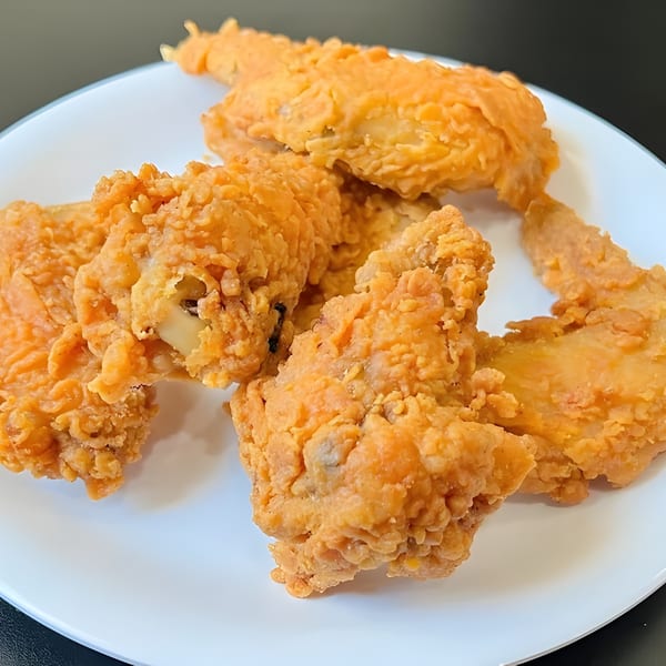 Crispy golden-brown fried chicken pieces, including wings and drumsticks, arranged on a white plate.