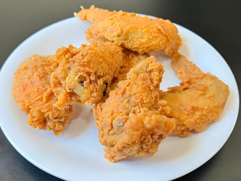 Crispy golden-brown fried chicken pieces, including wings and drumsticks, arranged on a white plate.