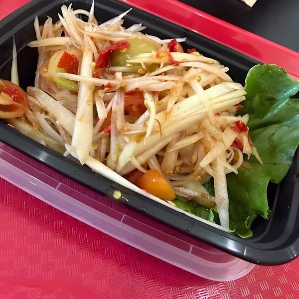 A close-up of a vibrant papaya salad with tomatoes and lettuce in a black to-go container.