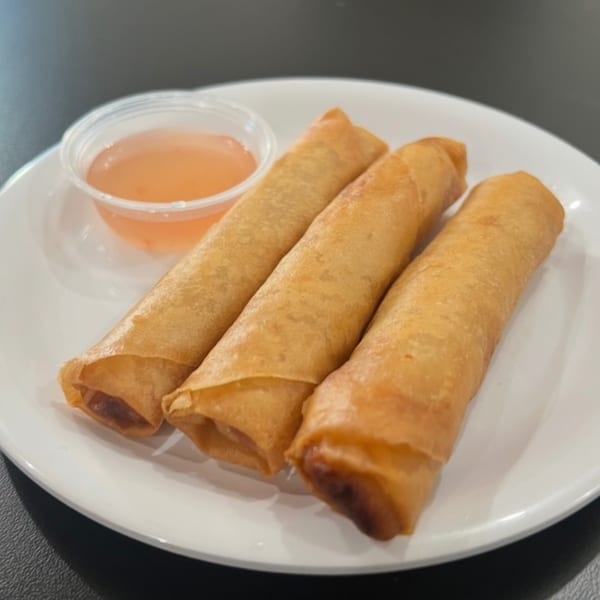 Three golden-brown spring rolls on a white plate with a side of sweet chili dipping sauce.