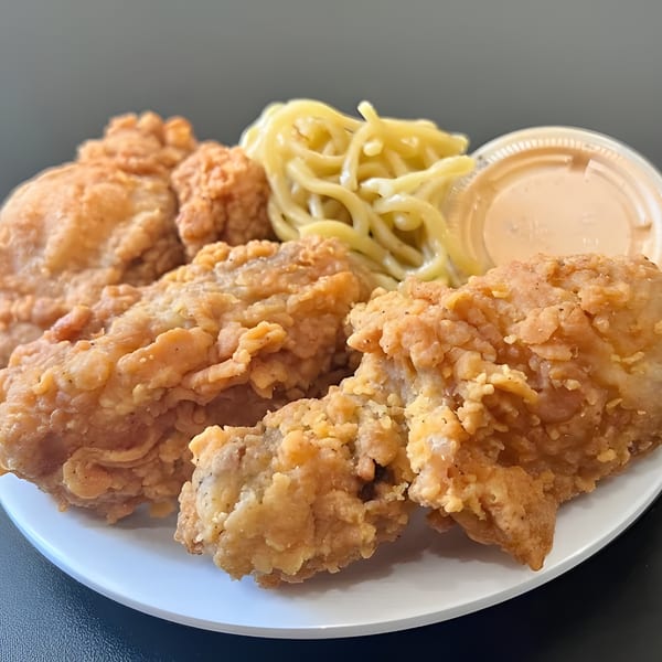 Crispy fried chicken pieces, a side of mac and cheese, and dipping sauce on a white plate.