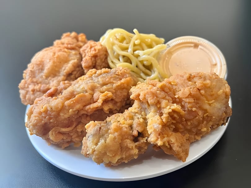 Crispy fried chicken pieces, a side of mac and cheese, and dipping sauce on a white plate.