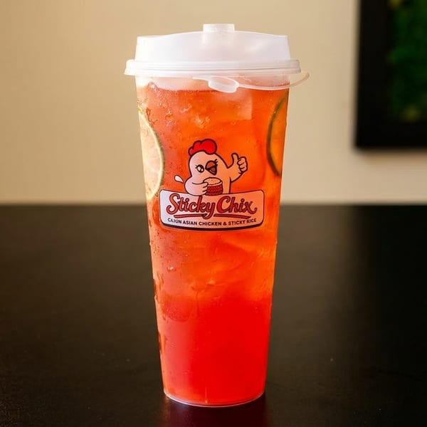 A tall, clear plastic cup of red iced tea with lime slices and the Sticky Chix logo.