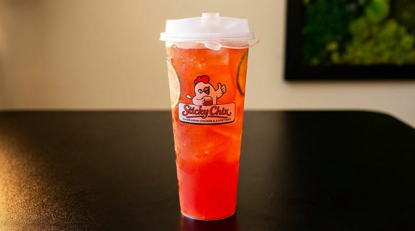 A tall, clear plastic cup of red iced tea with lime slices and the Sticky Chix logo.