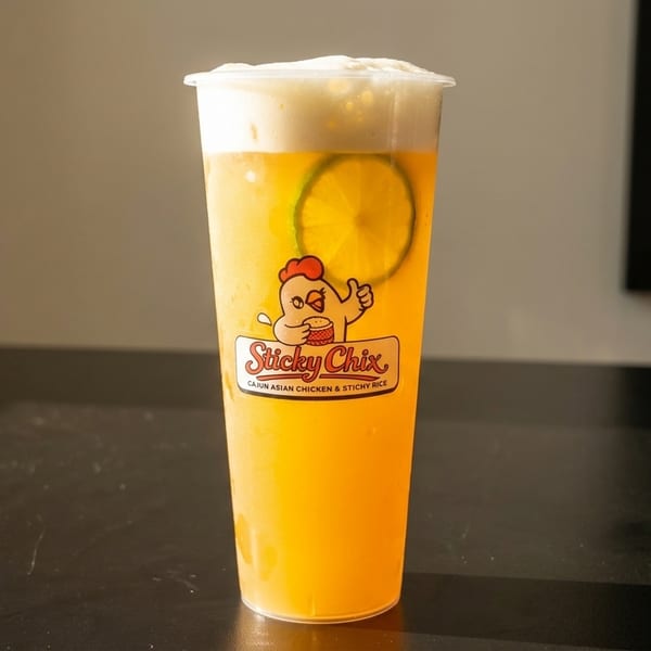 A tall plastic cup of yellow iced tea with a lime slice and foam, featuring the Sticky Chix logo.
