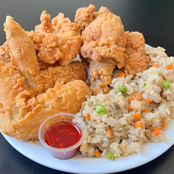 Crispy fried chicken pieces and fried rice with peas and carrots, served with a side of red sauce.