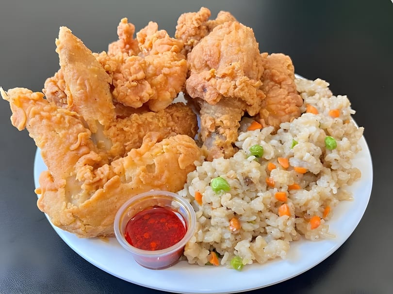 Crispy fried chicken pieces and fried rice with peas and carrots, served with a side of red sauce.