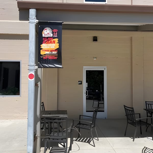 Outdoor patio seating with black tables and chairs outside a building with a restaurant banner.