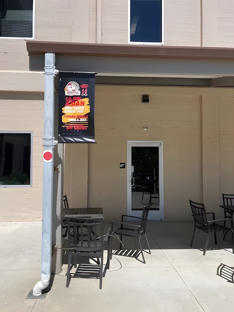 Outdoor patio seating with black tables and chairs outside a building with a restaurant banner.