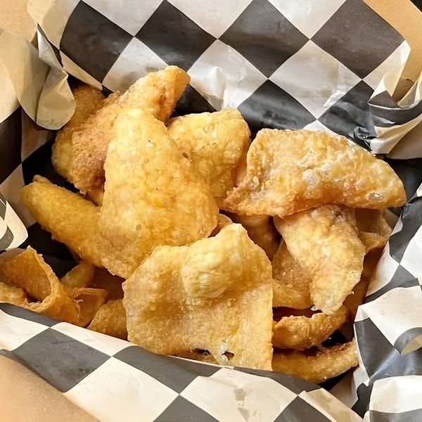 Crispy, golden fried pork rinds in a paper-lined basket with black and white checkered wax paper.