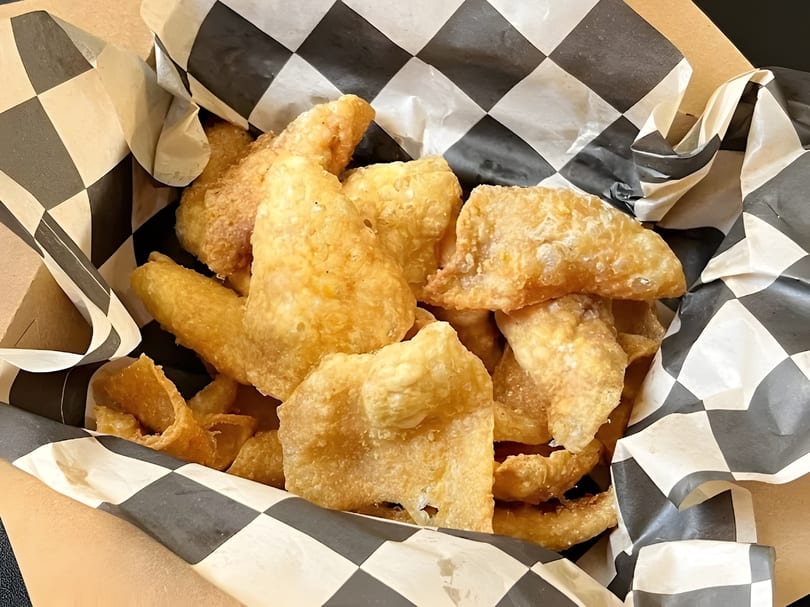 Crispy, golden fried pork rinds in a paper-lined basket with black and white checkered wax paper.