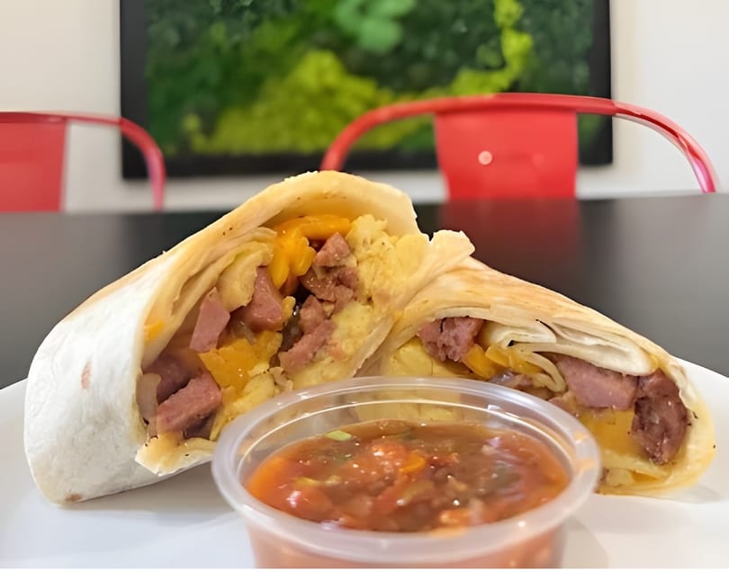 Breakfast burrito filled with scrambled eggs, sausage, and cheese, served with a side of salsa.